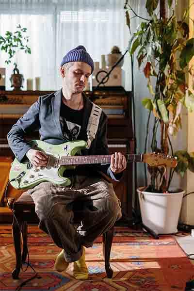 A man sitting on a chair in front of a piano, playing guitar